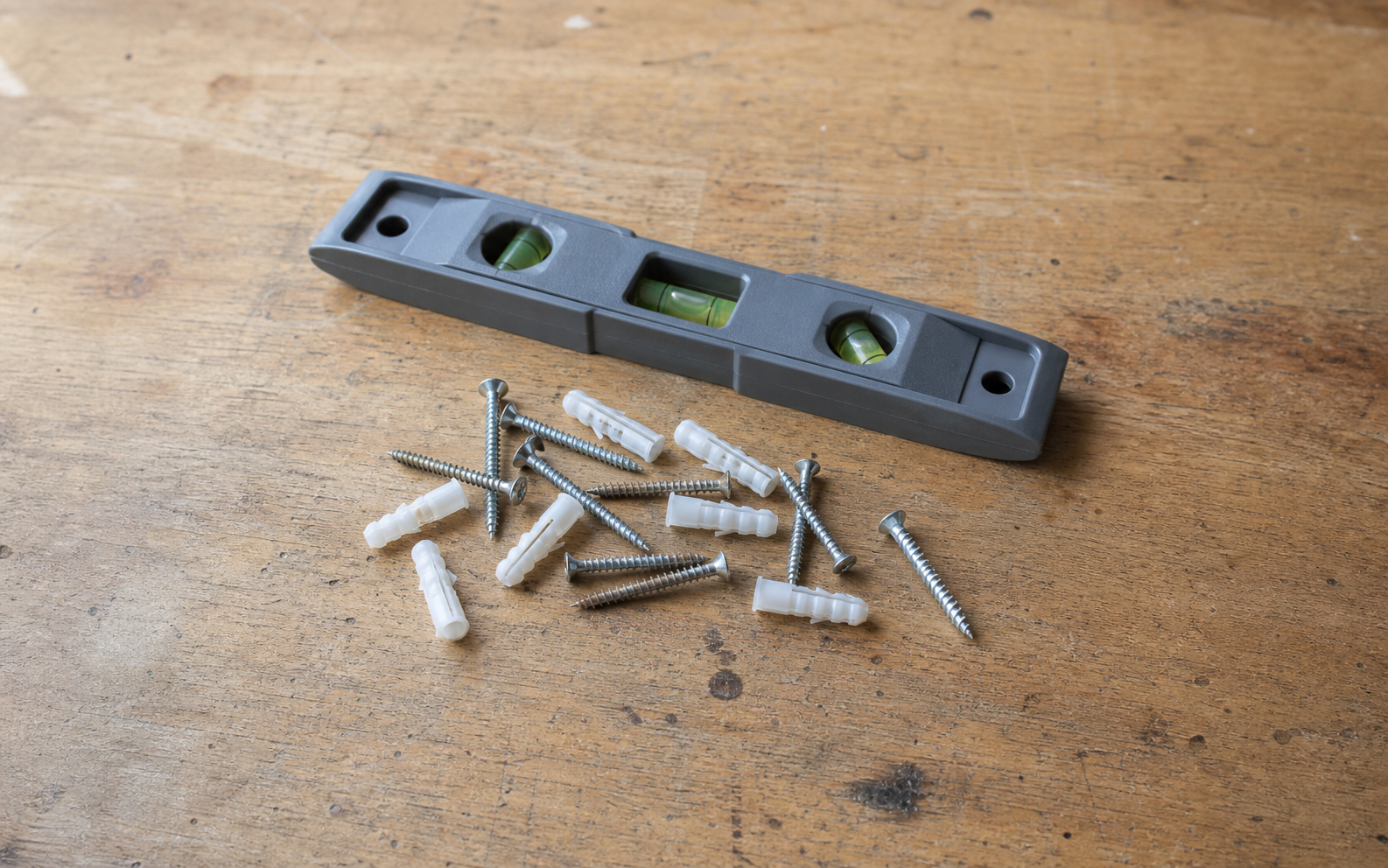Loose generic wall anchors and screws beside a plain level on a wood surface.